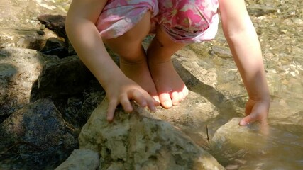 Close-up of a 4 year old caucasian child girl standing on rock in natural stream in summer and playing with stones. Seen in Germany in June.