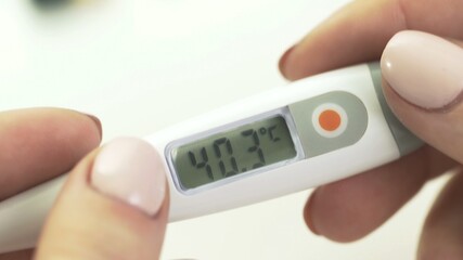 Slide shot of medical digital thermometer in womans hands 40.3
