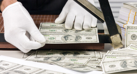 Counterfeiter cuts dollars printed on a cutter. Manufacturing of US dollars.