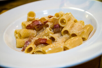 Carbonara rigatoni pasta with eggs, parmesan cheese, pepper and bacon. Typical seasoned italian pasta. High key narrow focus close up image