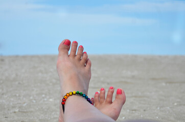 Woman feet with painted nails and bracelet on the beach