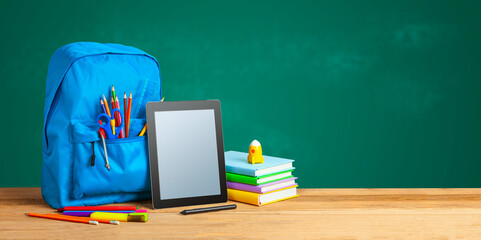 Back to school. Tablet and backpack with an supplies on the background of blackboard