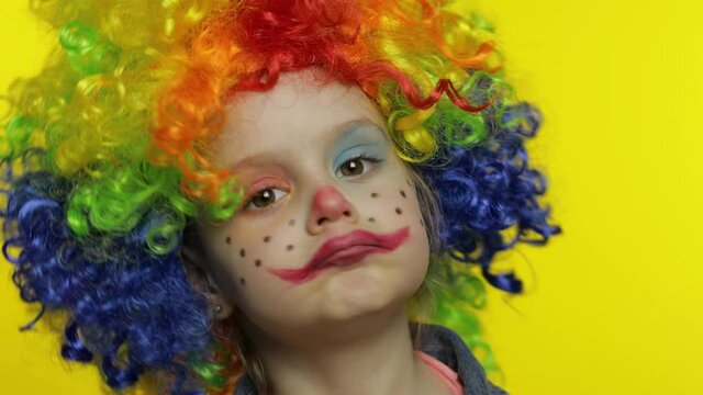 Little child girl clown in colorful wig tells something interesting. Having fun, smiling. Halloween