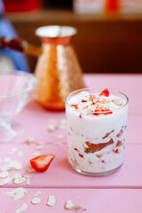 layered summer dessert with strawberries, sponge cake and yogurt on a pink tree background.