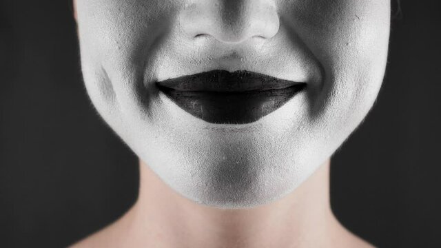 Portrait of a mime and bodypainting woman in white with black lips. Woman's lips on black background close-up