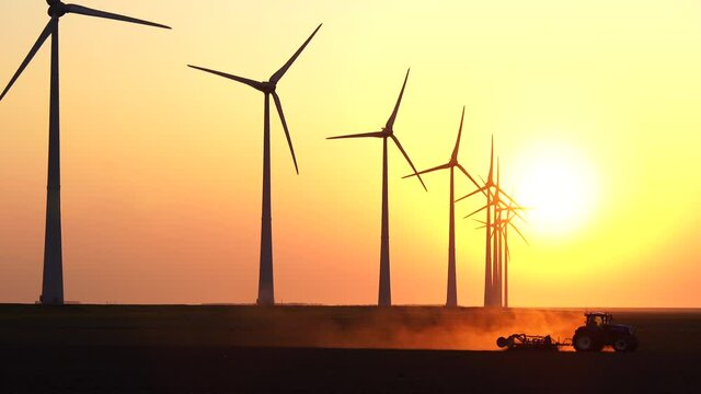 A tractor cultivating farmland during sunset at a row of windturbines. Groningen, Holland