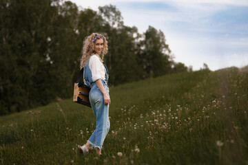 Fototapeta premium girl with curly hair and in denim overalls goes uphill on green grass