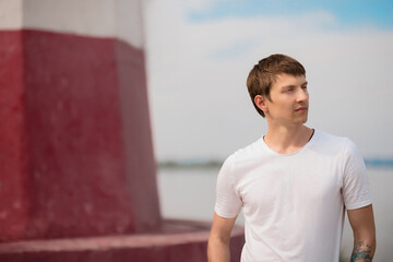 Obraz premium a guy in a white T-shirt stands on the street in the summer and looks away 