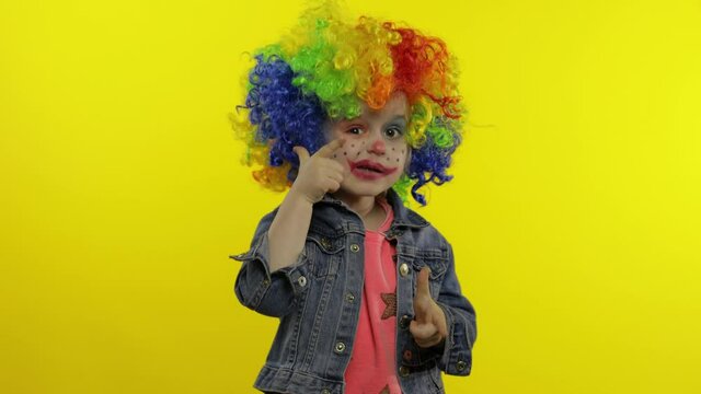 Little child girl clown in rainbow wig making silly faces, singing, smiling, dancing. Halloween
