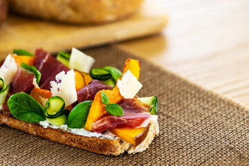 Open faced sandwich with iberico ham, parmesan cheese, goat cheese, zucchini, pumpkin, basil and chives on sourdough bread. All on a natural string textile, aside sourdough bread loaf. Copy space.