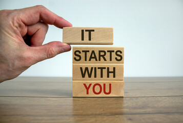 Male hand placing a block with word 'it' on top of a blocks tower with words 'starts with you'....