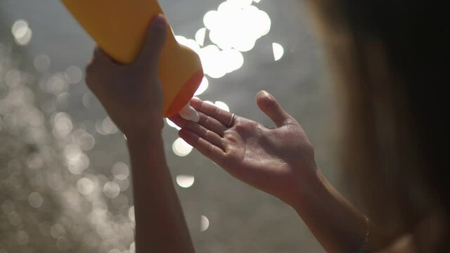 Woman squeezes sunscreen from a tube on her hand.