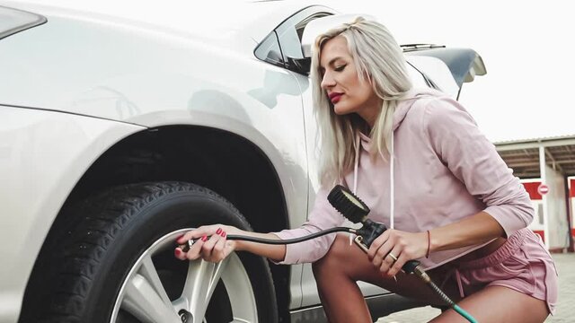 Hot sexy tanned woman pumps the wheel on an expensive car. The girl shakes the wheel with the pump. Beautiful professional model with white hair.