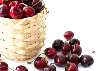 Ripe cherry berries in the wooden basket isolated on the white background. Some berries are scattered around. Copy space. Selective focus