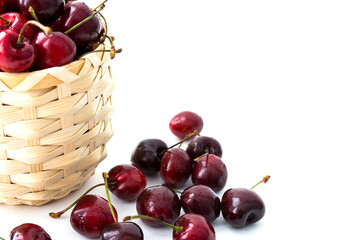Ripe cherry berries in the wooden basket isolated on the white background. Some berries are scattered around. Copy space. Selective focus