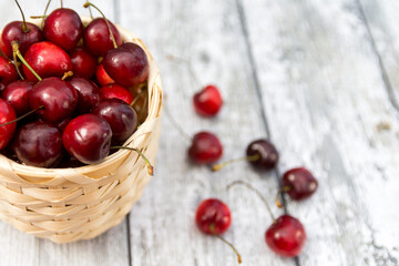 Closeup photo of a wooden basket with ripe cherries on the wooden background. Selectibe focus
