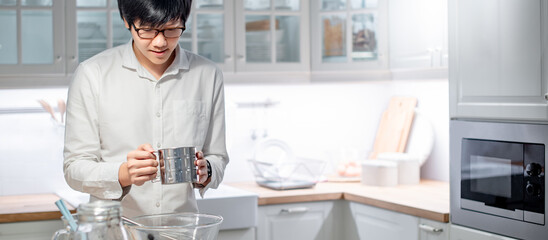 Asian man cooker holding stainless steel flour sifter preparing baking utensils on counter in the kitchen. Cooking concept