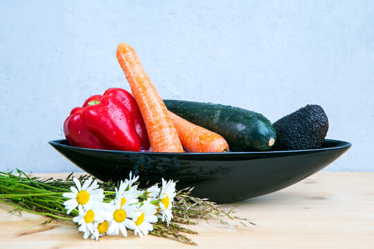 avocado, bell pepper, carrots and cougette in black bowl on wooden table with daisies