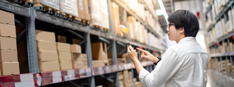 Asian man shopper standing in warehouse inventory aisle checking shopping list on smartphone. Buying or purchasing factory goods. Shopaholic concept