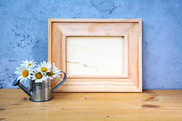 wooden picture frame on table with miniature watering can and daisies