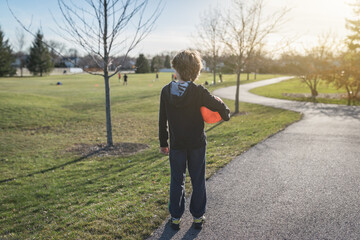 Rear view of a child holding a bright orange soccer ball in a park