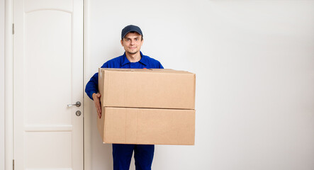 Young happy delivery man in blue uniform is shipping a parcel for the client.