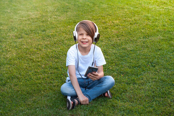 a boy on the green grass and listens to music on headphones