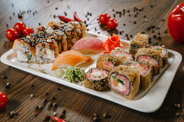 Rolls and sushi on a plate surrounded by vegetables and spices. The serving of the meal