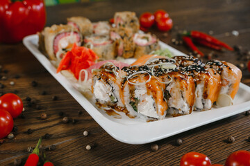 Rolls and sushi on a plate surrounded by vegetables and spices. The serving of the meal