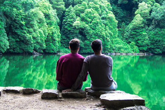 Romantic young gay couple sitting in a beautiful landscape with lake and mountains in a calm moment