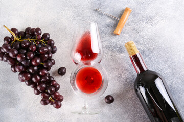 Flat lay composition with two glasses of vintage red wine, bunch of grapes & corkscrew on grunged concrete table background. Expensive bottle of cabernet sauvignon concept. Copy space, top view.