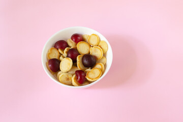 White bowl with cereal tiny pancake with sweet cherry on a pink background. Copy space. Trendy food concept.