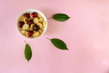 White bowl with a tiny pancake flakes with sweet cherry and green leaves on a pink background. Top view. Trendy food concept.