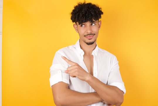 Portrait of young man posing on camera with tricky look and gesturing to side. Male designer presenting lovely product with index finger. Gesture concept.