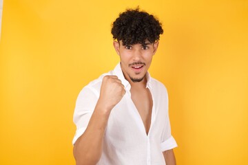 Fierce confident European dark-haired man holding fist in front of him as if is ready for fight or challenge, screaming and having aggressive expression on face. Isolated over gray background.