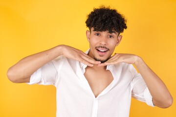 Pretty surprised male in white T-Shirt fooling around in studio and jumping. Adorable guy dancing on colorful background and touching chin with hands having good time.