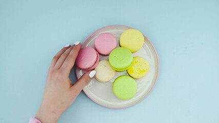 Sweet color macaroons or macaron in white plate on pastel blue surface.