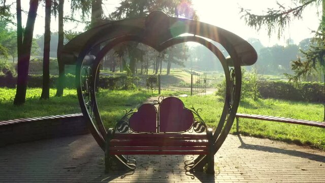 Gazebo Arbor Altanka for lovers: a bench under the roof with two hearts. Zoom Out Crane Shot. Arbor of lovers in the park among the trees in the summer.