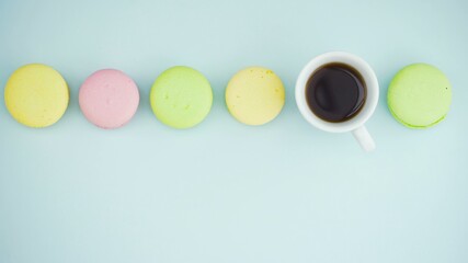 Macaroons or macaron on pastel blue surface with espresso in white cup.