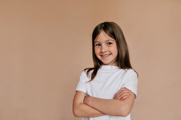 Happy lovable girl wearing white t-shirt posing over beige background. Adorable baby girl stand joyfully on beige background