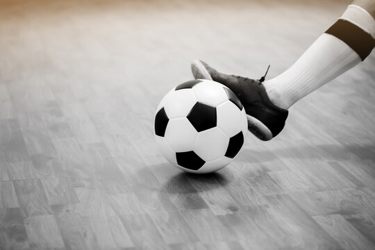 Black and white image of Futsal ball with motion blurry futsal player run and contol ball to shoot  to goal on wooden floor in sports hall. Youth futsal league. Soccer game indoor.