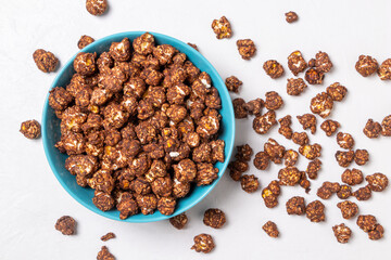 Chocolate popcorn in a blue cup isolated on light background. Sprinkled popcorn is next to the cup.