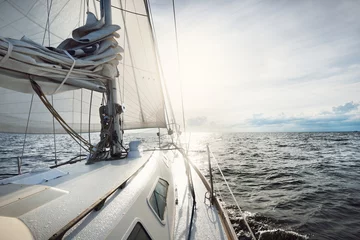 Fotobehang White yacht sailing in an open sea on a sunny summer day. Close-up view from the deck to the bow and sails. Waves and water splashes. Clear blue sky with cirrus clouds and plane tracks. Netherlands © Alex Stemmer