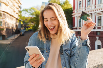 Cheerful young blonde girl shopping online with mobile phone