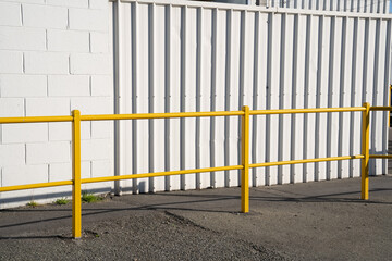 Yellow fences for walkway close to white wall of factory.
