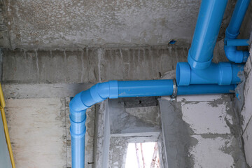 blue water tube install on concrete white wall for building restroom in house site. fixing pipe for maintenance in service ceiling.