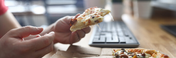 Man eating pizza in workplace in front computer