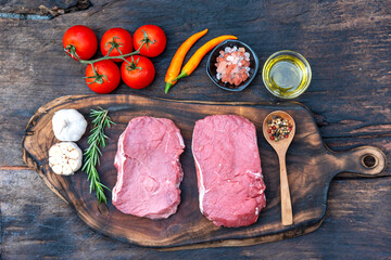 Raw meat beef steak organic fresh ingredient on wooden board table background in kitchen with rosemary, salt, garlic, tomato, black pepper, olive oil. Meat beef on wooden plate for beefsteak raw meat