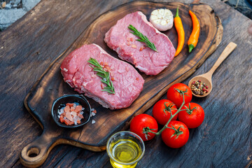 Raw meat beef steak organic fresh ingredient on wooden board table background in kitchen with rosemary, salt, garlic, tomato, black pepper, olive oil. Meat beef on wooden plate for beefsteak raw meat