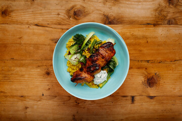 A delicious bowl of  tandoori chicken, vegetables and rice, in a blue bowl shot on a rustic wooden background